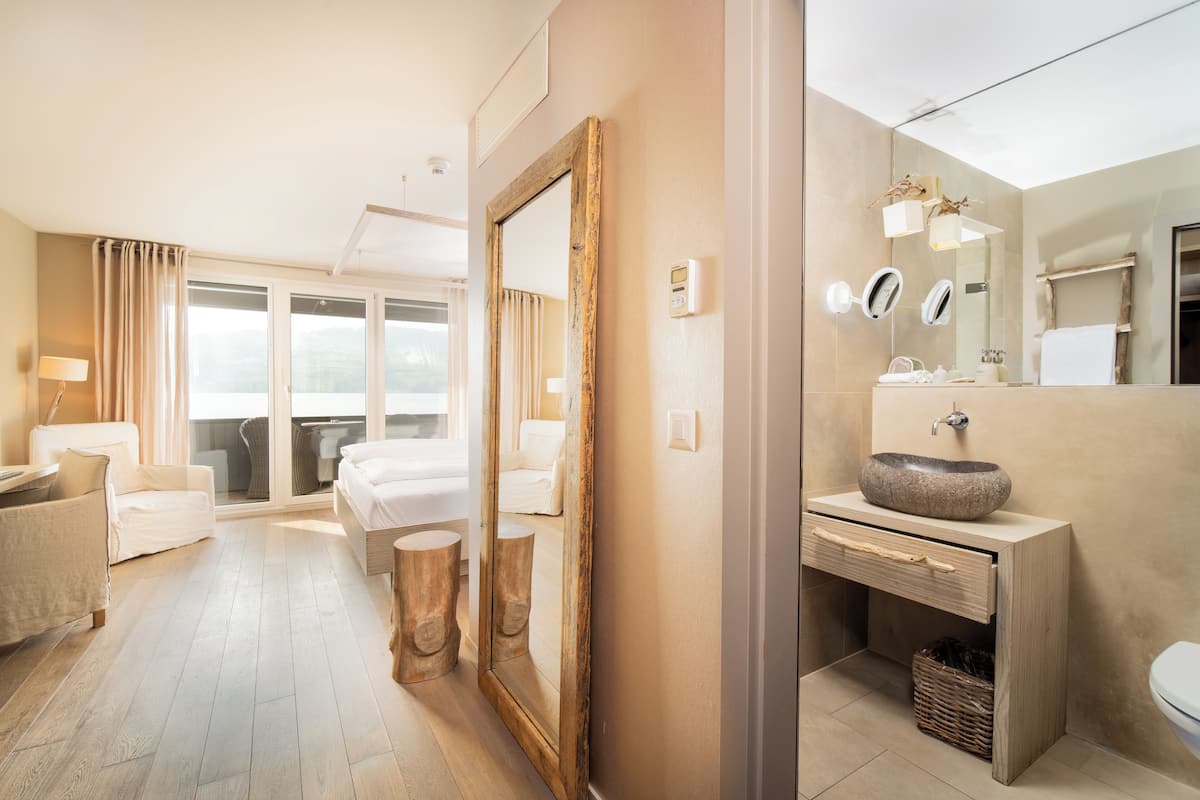 Ein Hotelzimmer mit großem Spiegel, einem Holznähefrisiertisch, einem Bett, einem Sofa und Blick ins Freie.