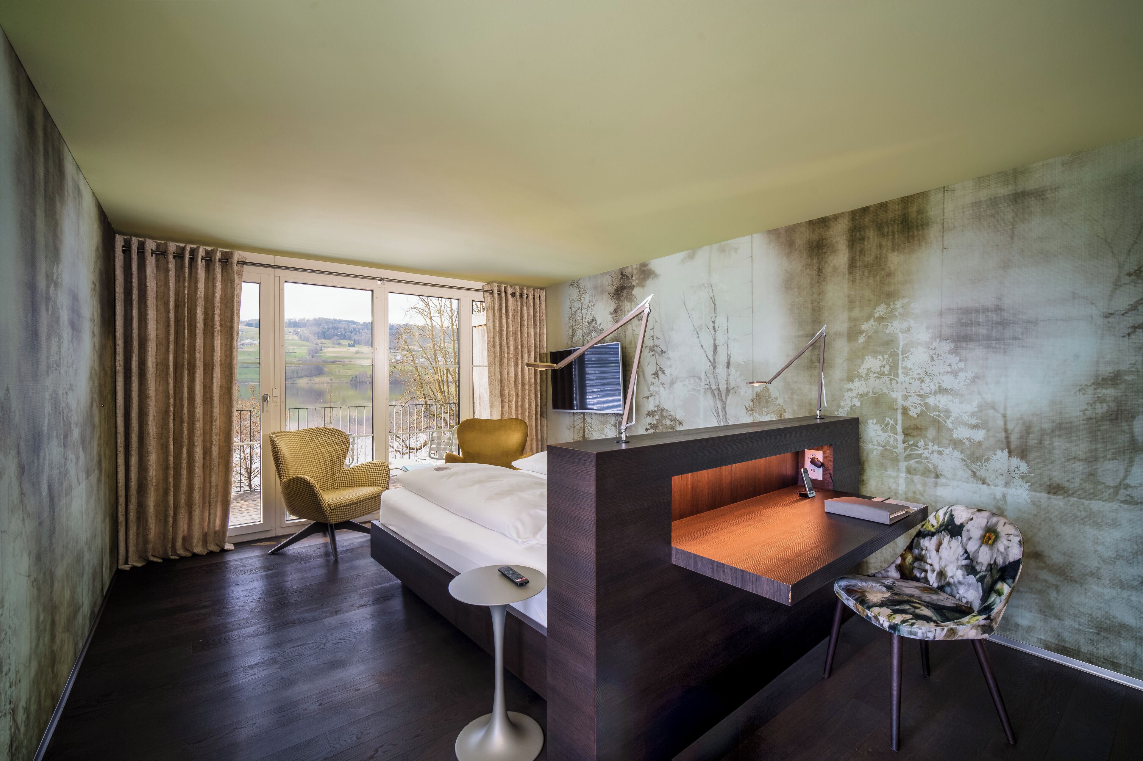 Habitación de hotel con cama, escritorio, silla, televisor y vista al exterior.