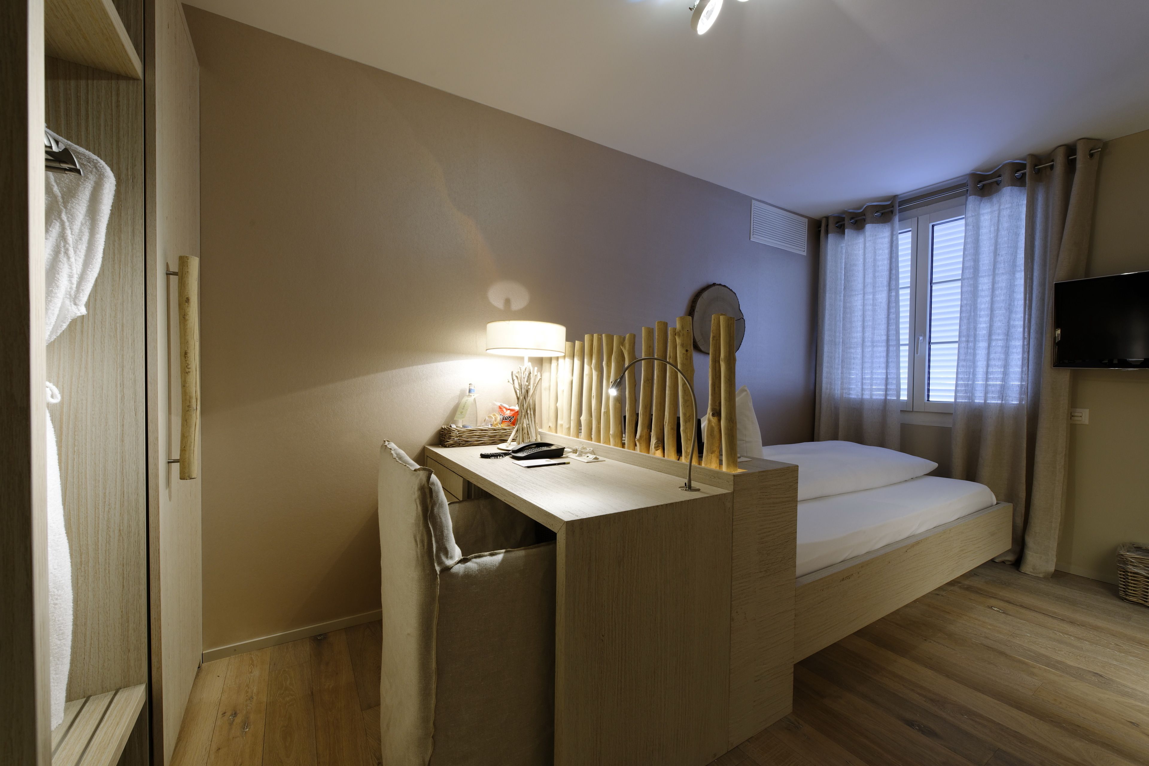 Une pièce de taille modeste comprenant un lit, un petit bureau avec une lampe, un miroir et un téléviseur.