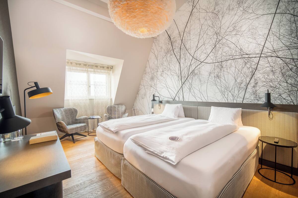 Ein modernes Hotelzimmer mit einem großen Bett, einem Schreibtisch, einem Sessel und einer Wand mit einem Ast-Design.