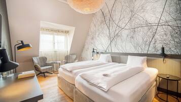 Moderni hotellihuone, jossa on suuri sänky, työpöytä, tuoli ja seinä, jonka kuvioinnissa on käytetty puun oksia.