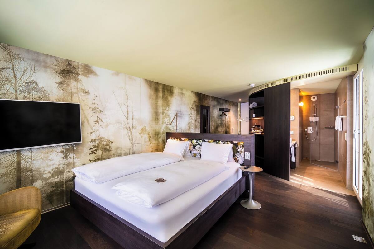 Ein Hotelzimmer mit einem großen Bett, einem Flachbildfernseher, Holzboden und Blick auf den Flur.