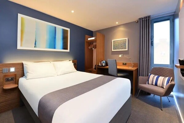 Een hotelkamer met een groot bed, een bureau, een stoel en een raam met gordijnen.