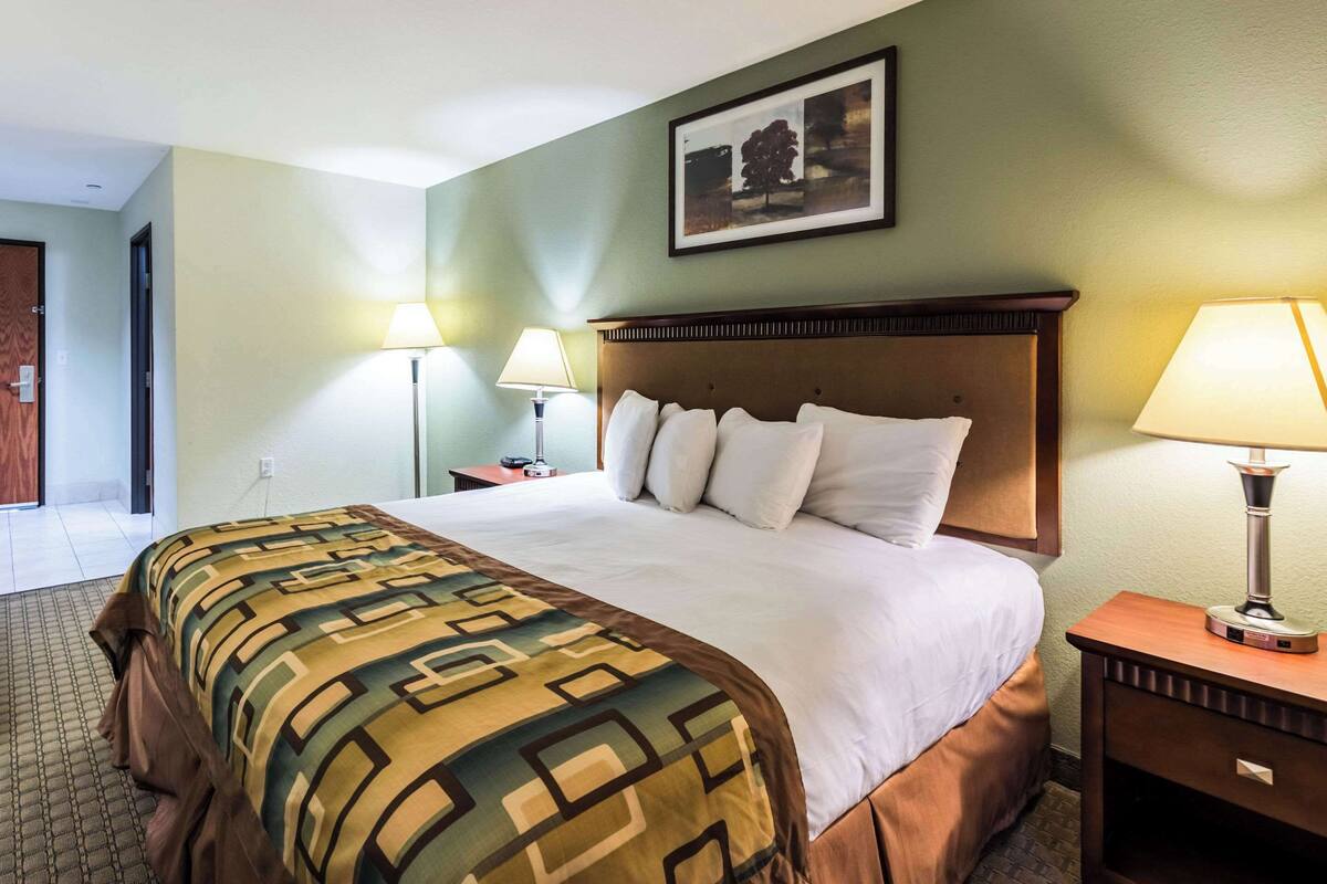 Une chambre d’hôtel avec un grand lit, deux lampes de chevet, une table de nuit en bois et un tableau encadré au mur.