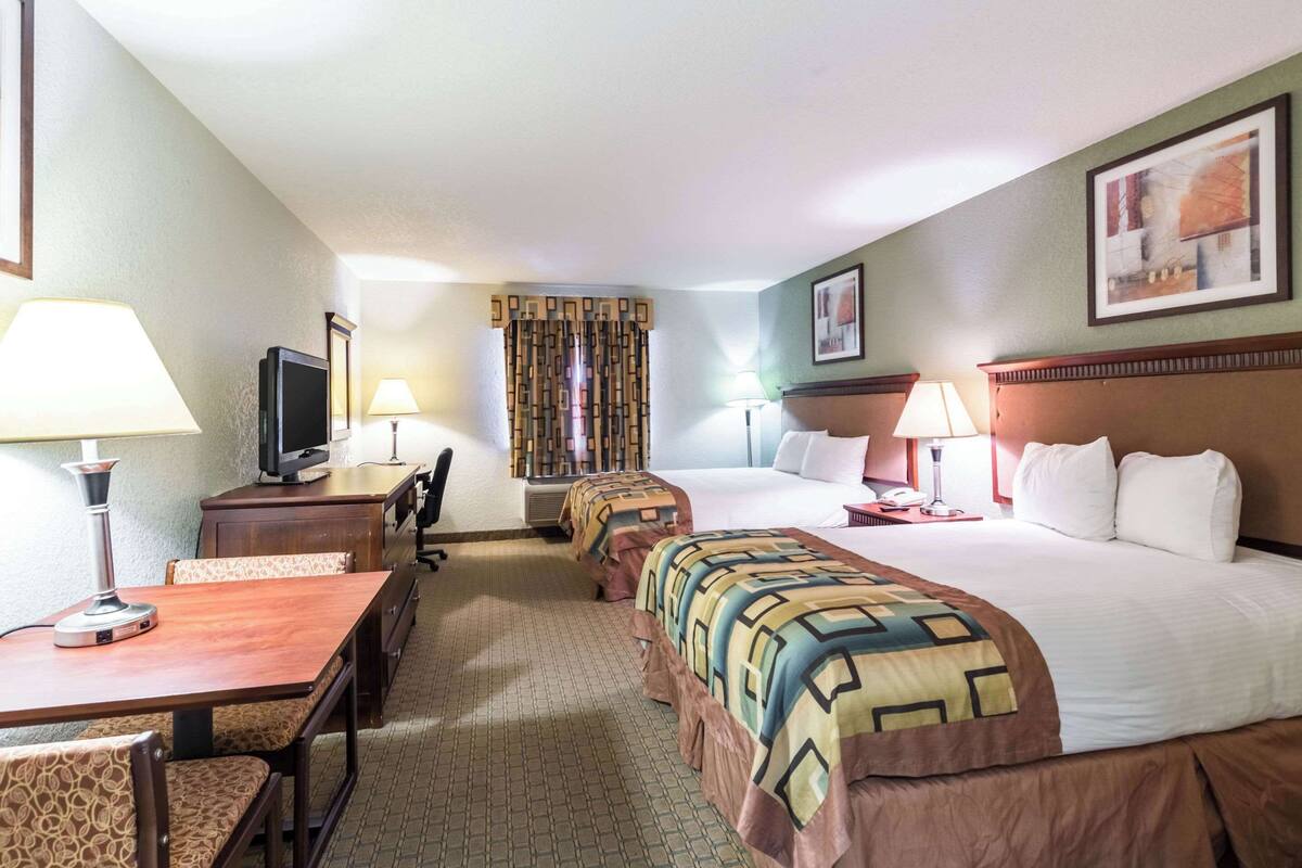 Une chambre d’hôtel avec deux lits, un bureau avec un ordinateur, une chaise, une télévision et une fenêtre avec des rideaux.