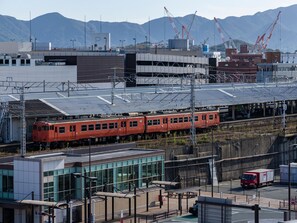 Una estación de tren con un tren rojo, edificios modernos y montañas al fondo.