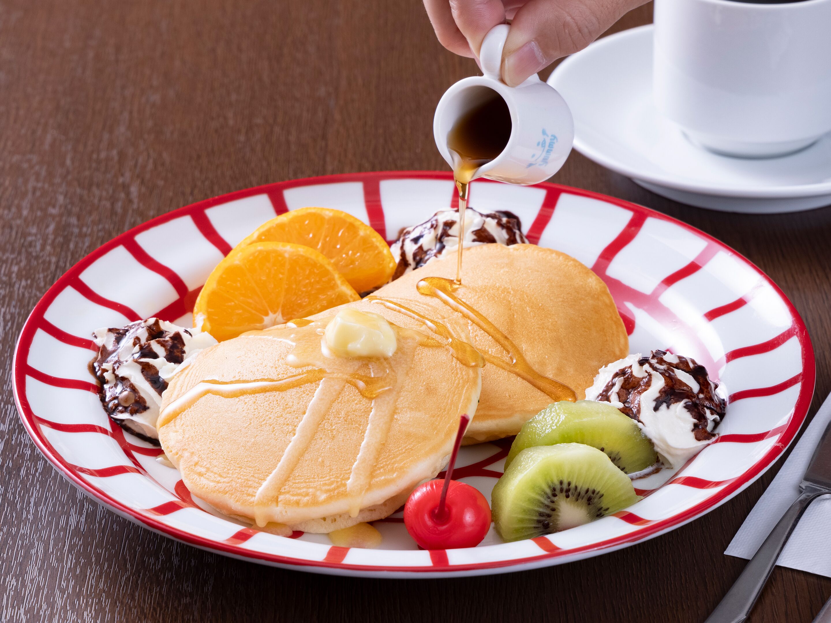 A plate with pancakes, syrup, whipped cream, and fruit.