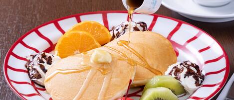 A plate with pancakes, syrup, whipped cream, and fruit.