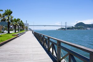 Um calçadão de madeira que leva a uma ponte sobre a água, com palmeiras e edifícios à esquerda.
