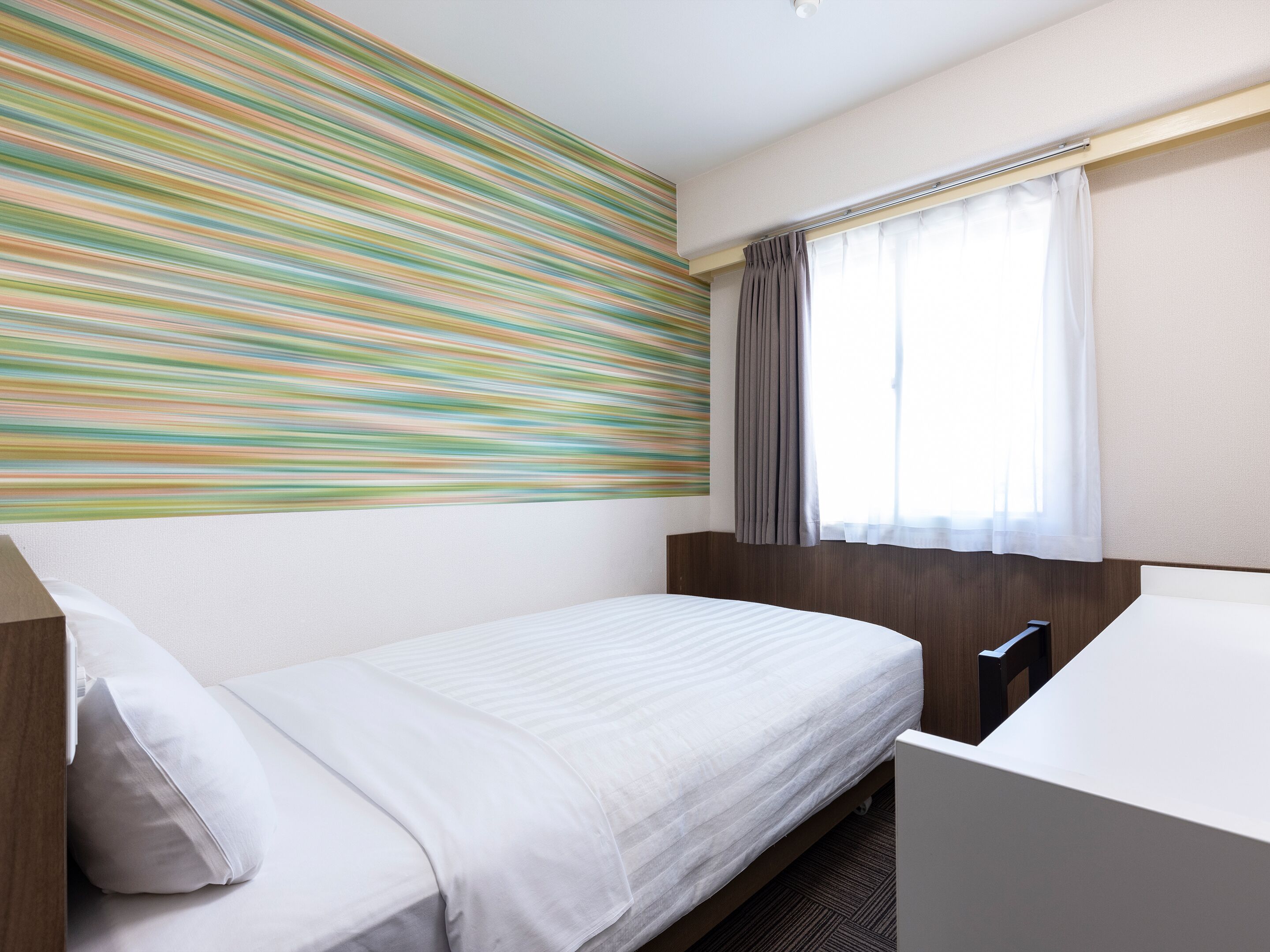 Une chambre d’hôtel avec un lit, une fenêtre avec des rideaux et un mur à rayures.