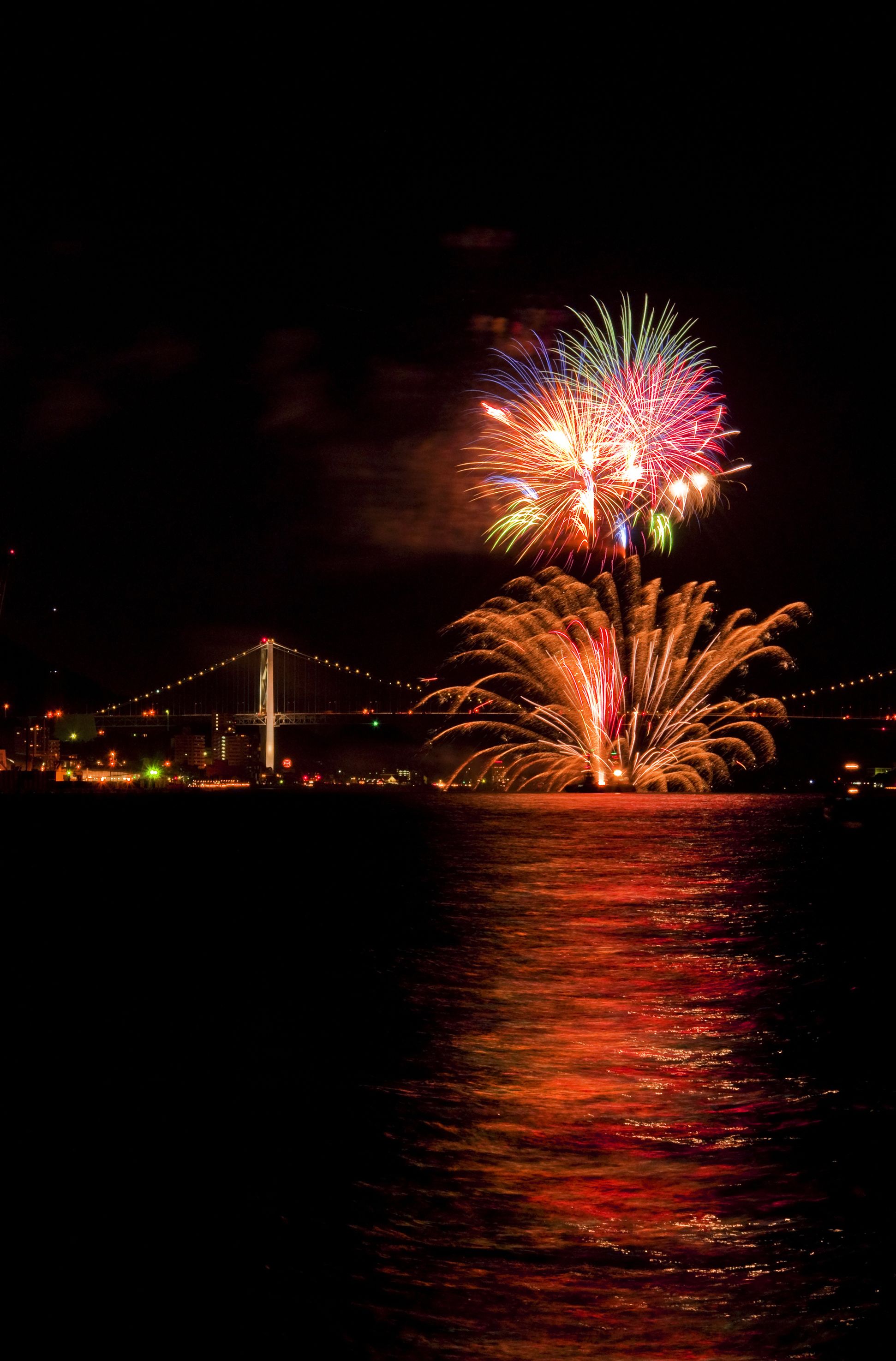 A nighttime view of a bridge with fireworks over water.