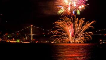 A nighttime view of a bridge with fireworks over water.