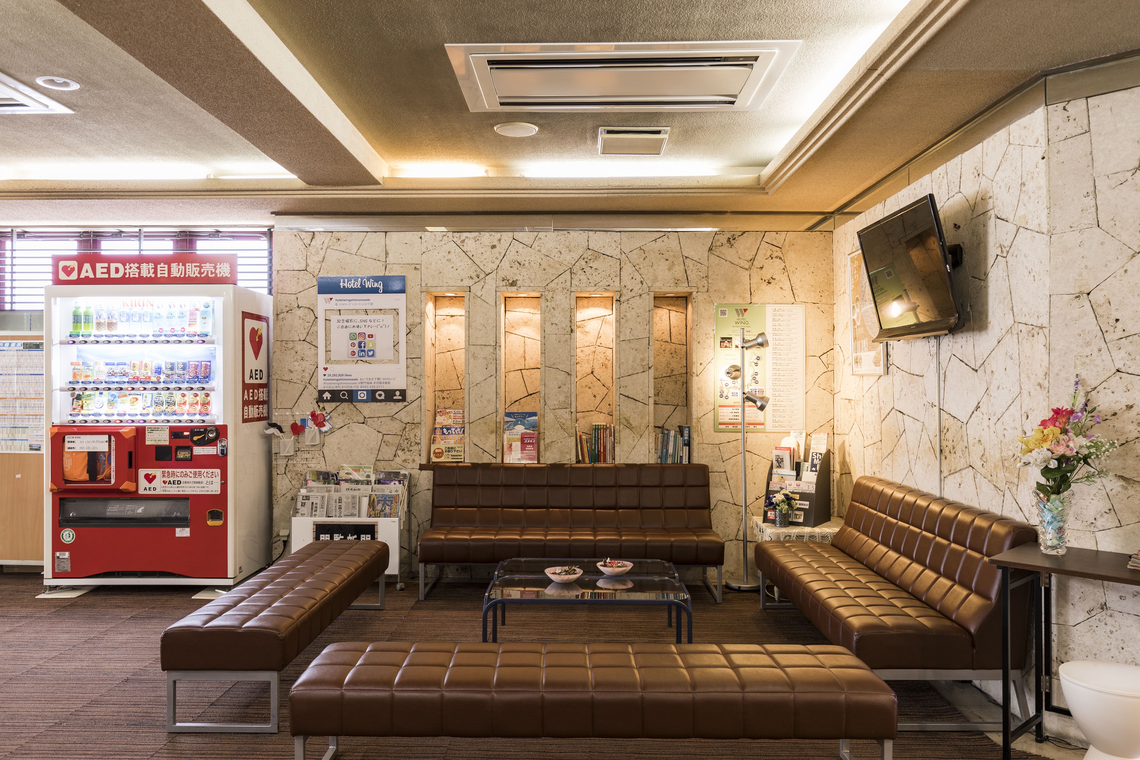 A hotel lobby with a brown leather sofa, a glass coffee table, a bench, and an AED machine.