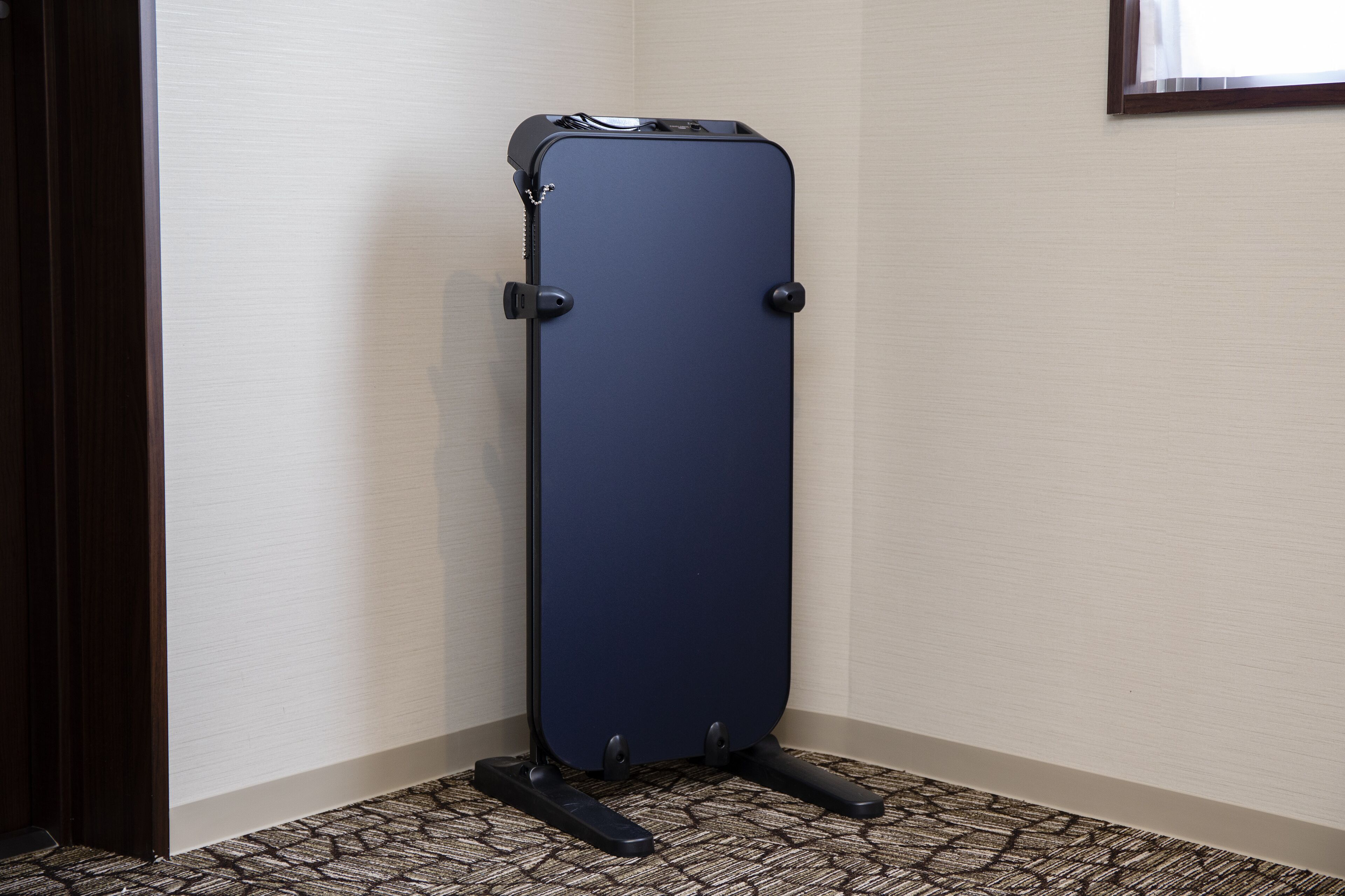 A corner room with a dark blue portable storage unit against a beige wall and patterned carpet.