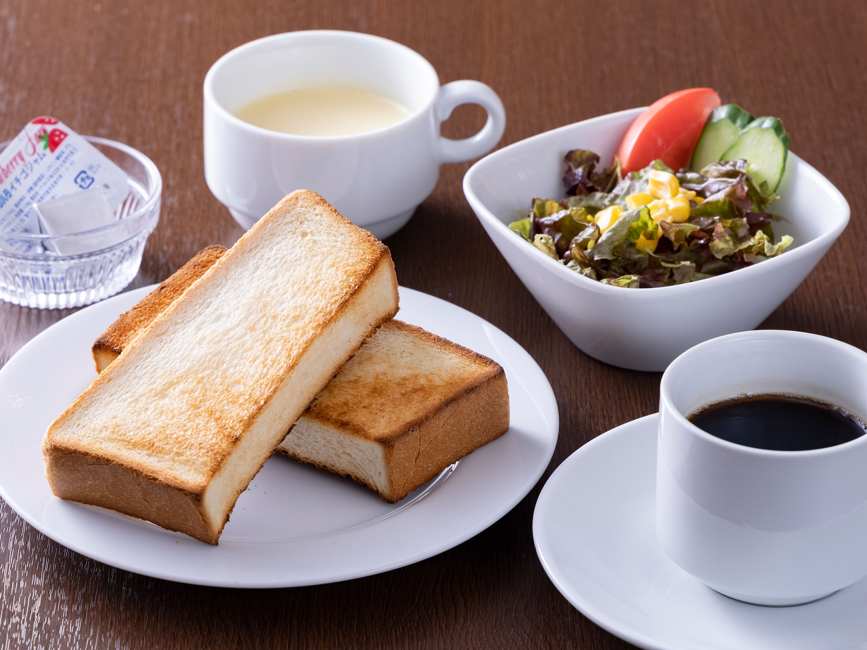 A breakfast setting with toast, a bowl of salad, a cup of coffee, and a glass of milk on a wooden table.