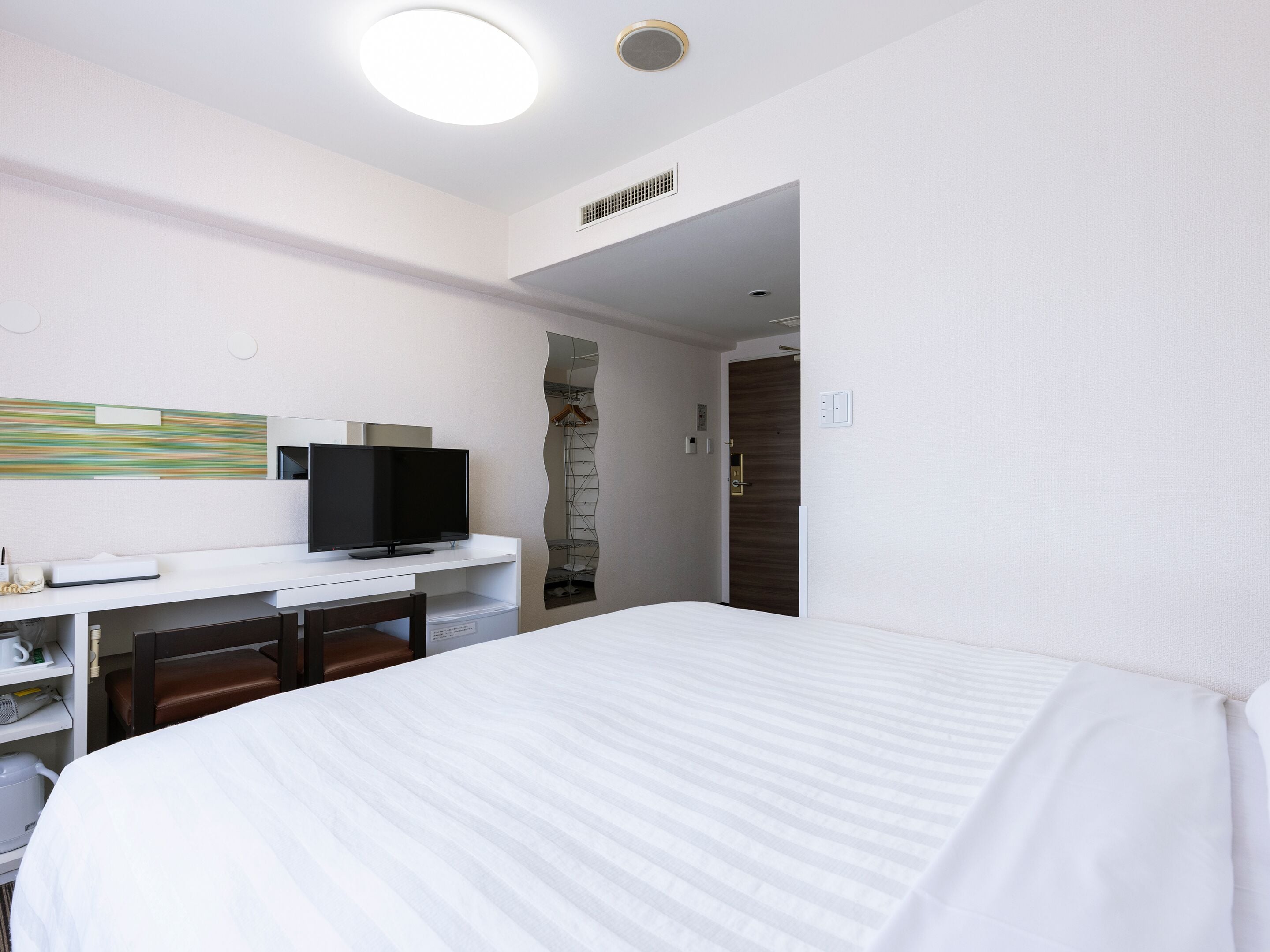 A hotel room with a bed, a desk with a television, and a wardrobe.