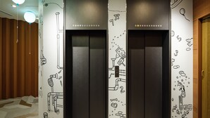 A modern elevator with black walls and white panels featuring black line drawings of various objects and numbers. - KOKO HOTEL Ikebukuro East (Tokyo)