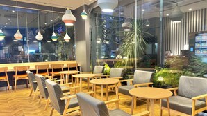 A modern cafe interior with wooden furniture, pendant lighting, and large windows offering views of the city. - KOKO HOTEL Ikebukuro East (Tokyo)