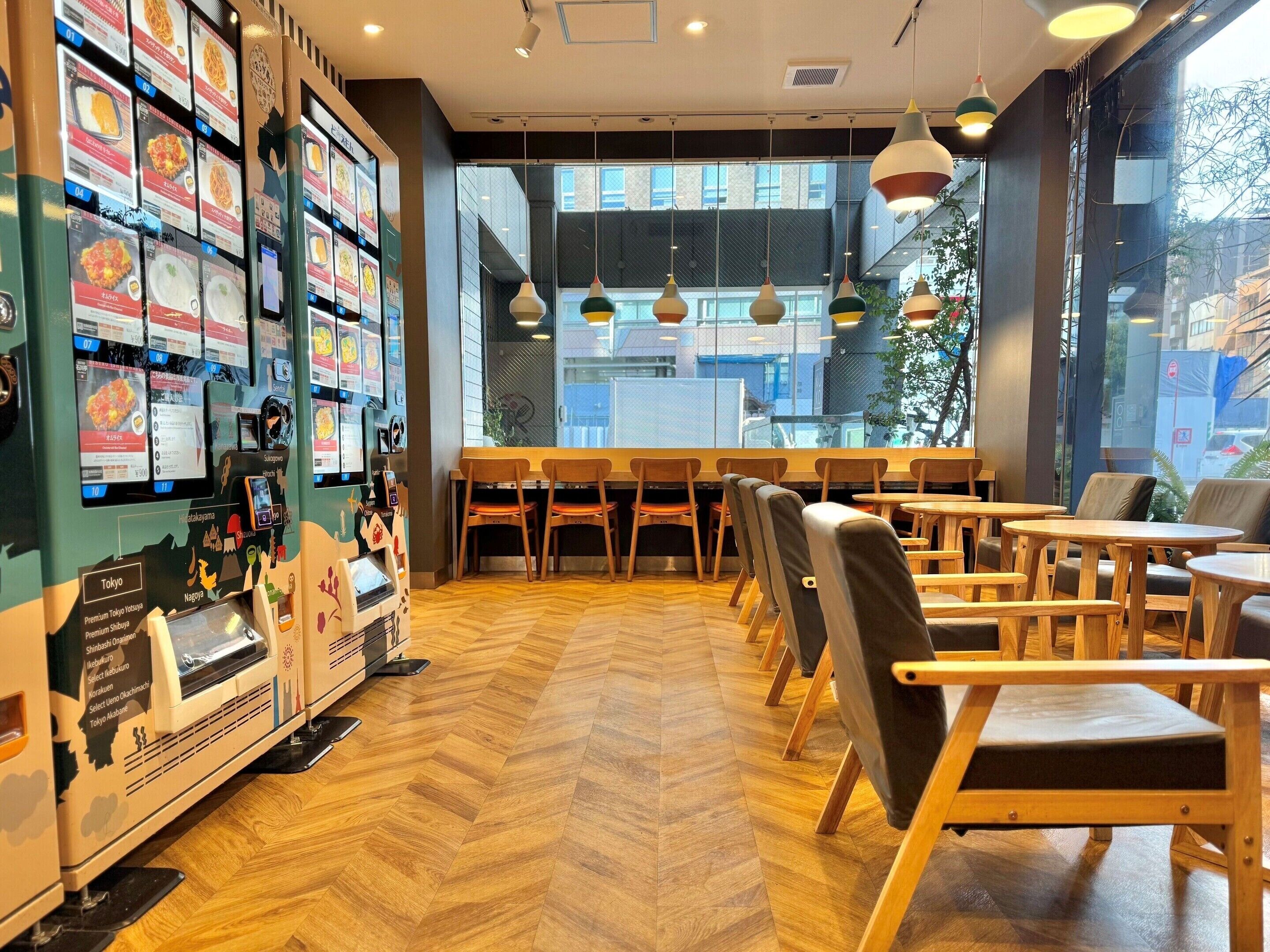 L’intérieur d’un restaurant, avec des chaises et des tables en bois, un présentoir pour le menu et de grandes fenêtres offrant une vue sur la ville.