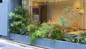 A modern building with a glass facade, a seating area with a table and chairs, and a variety of plants in a planter box. - KOKO HOTEL Ikebukuro East (Tokyo)