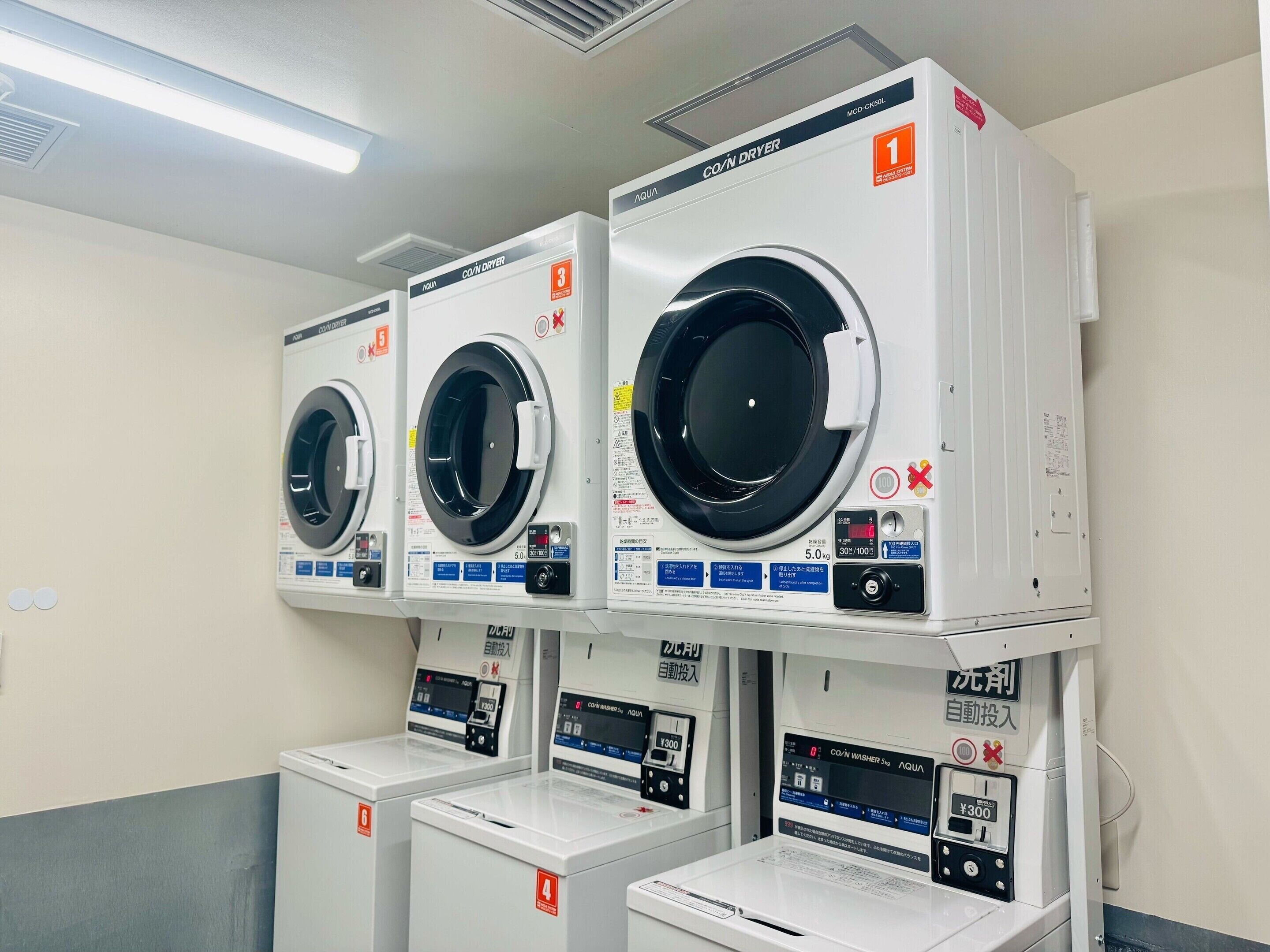 Een rij witte wasmachines met voorlader, bedieningspanelen en veiligheidslabels.