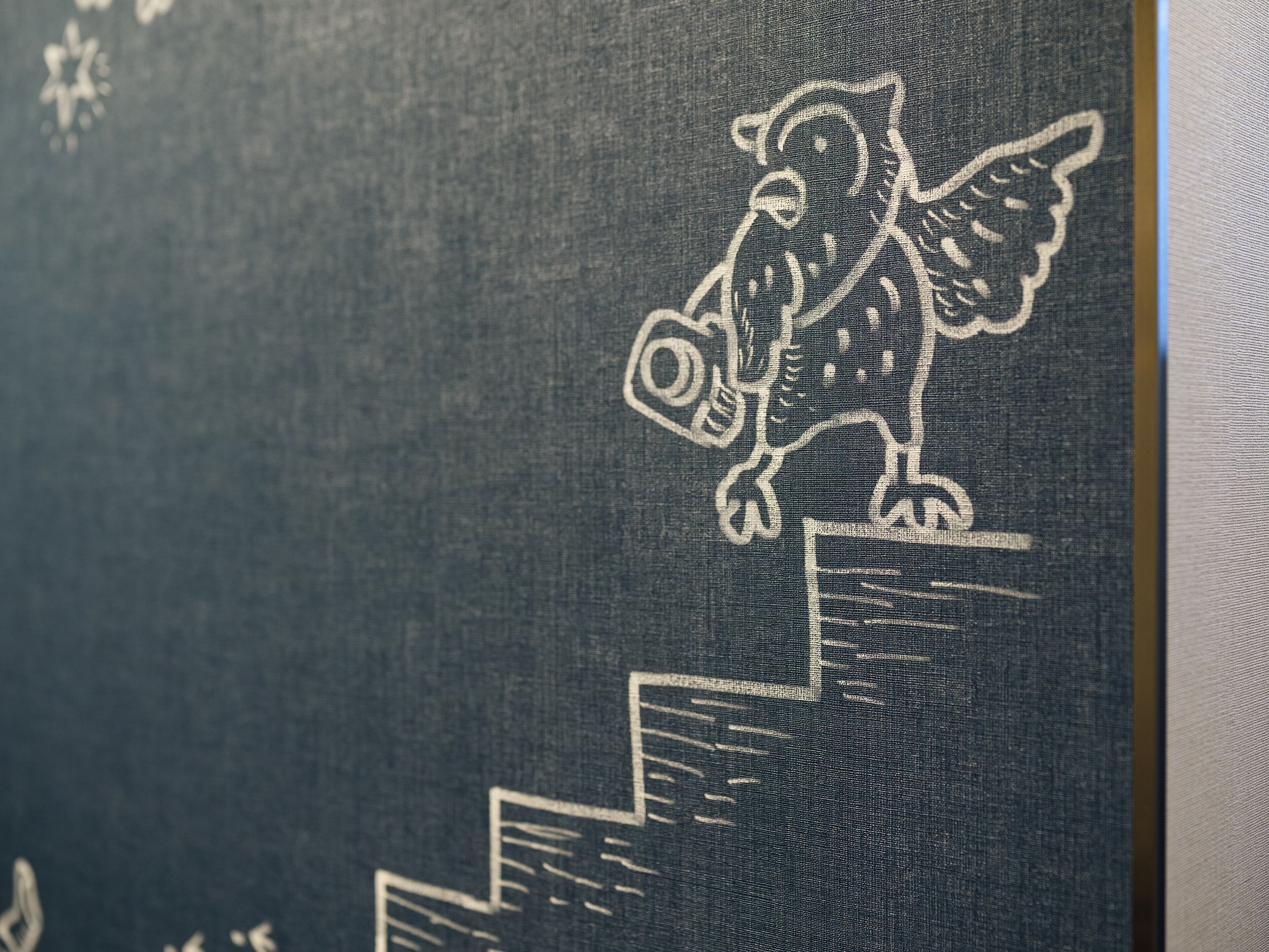 A close-up of a fabric with a white embroidered design of an owl holding a lantern, standing on a staircase.
