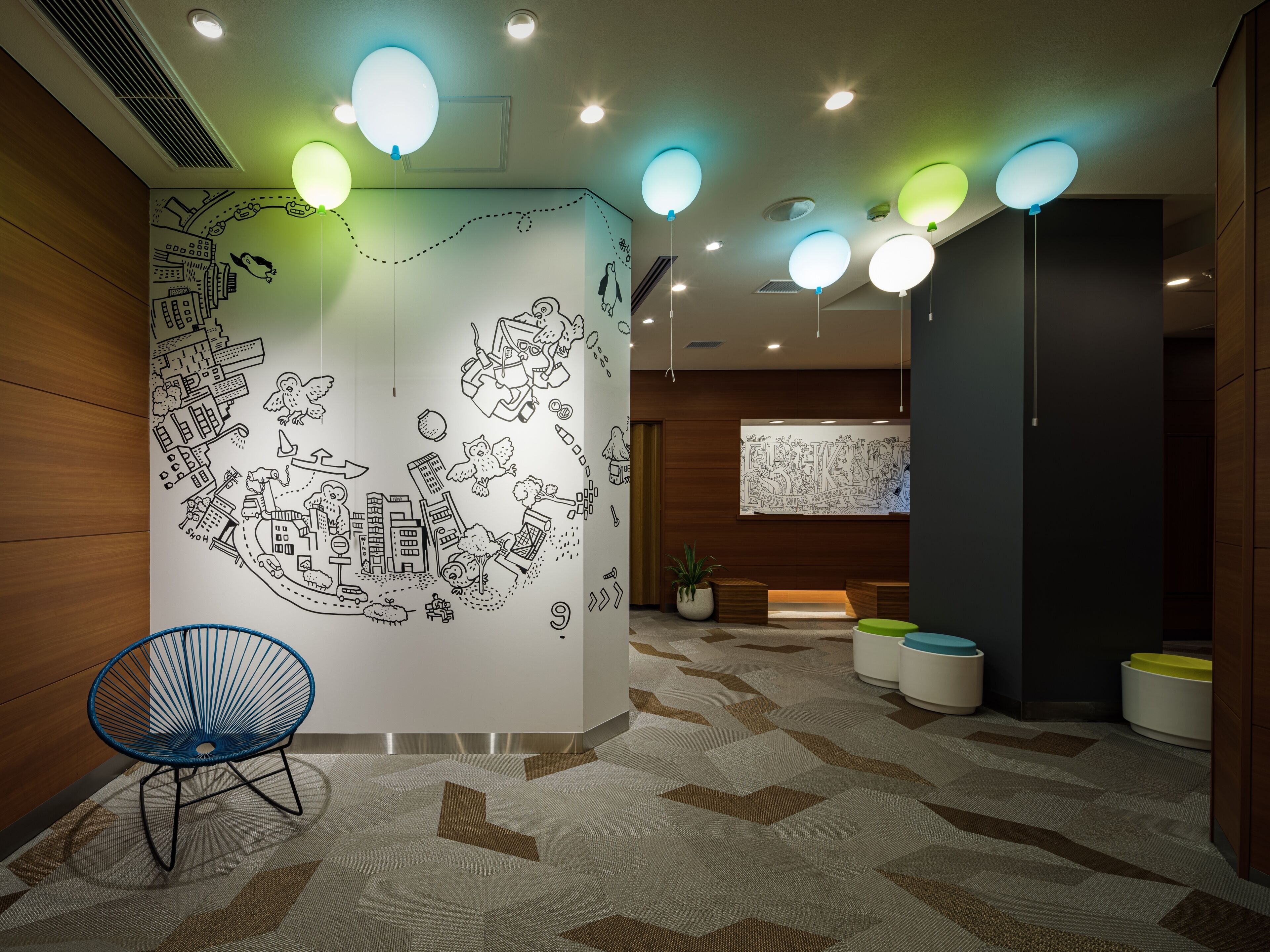 A hotel lobby with a large wall mural, a blue chair, and a geometric patterned carpet.