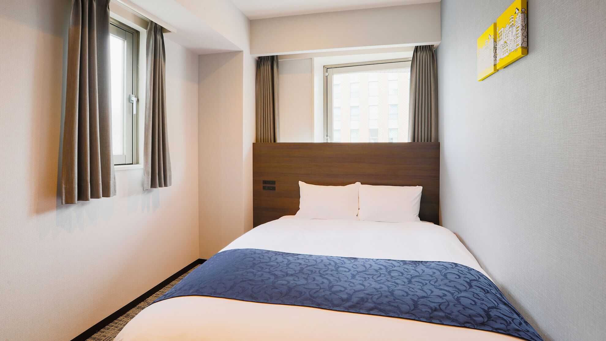 A hotel room with a large bed, a headboard, a window with curtains, and a wall-mounted artwork.