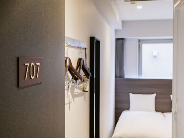 A hotel room with a bed, a coat rack with hangers, and a wall-mounted number sign '707'.
