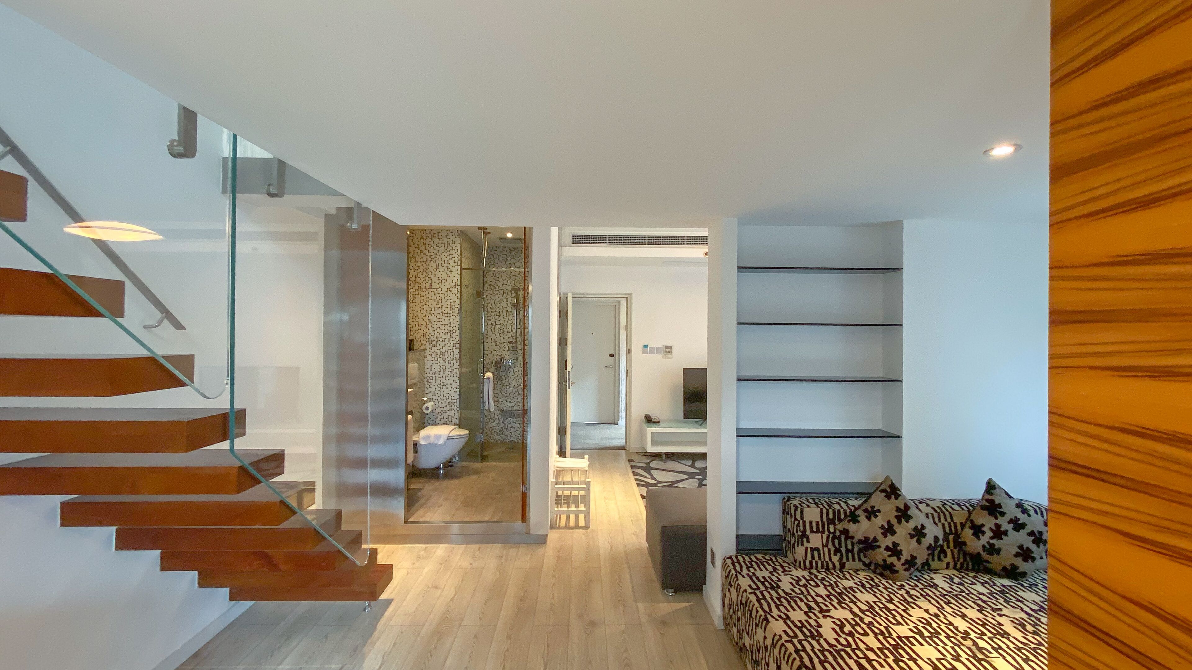 Un interior moderno con una escalera, un baño, una zona de estar y una estantería.