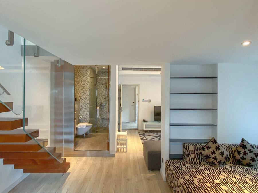 Un interior moderno con una escalera, un baño, una zona de estar y una estantería.