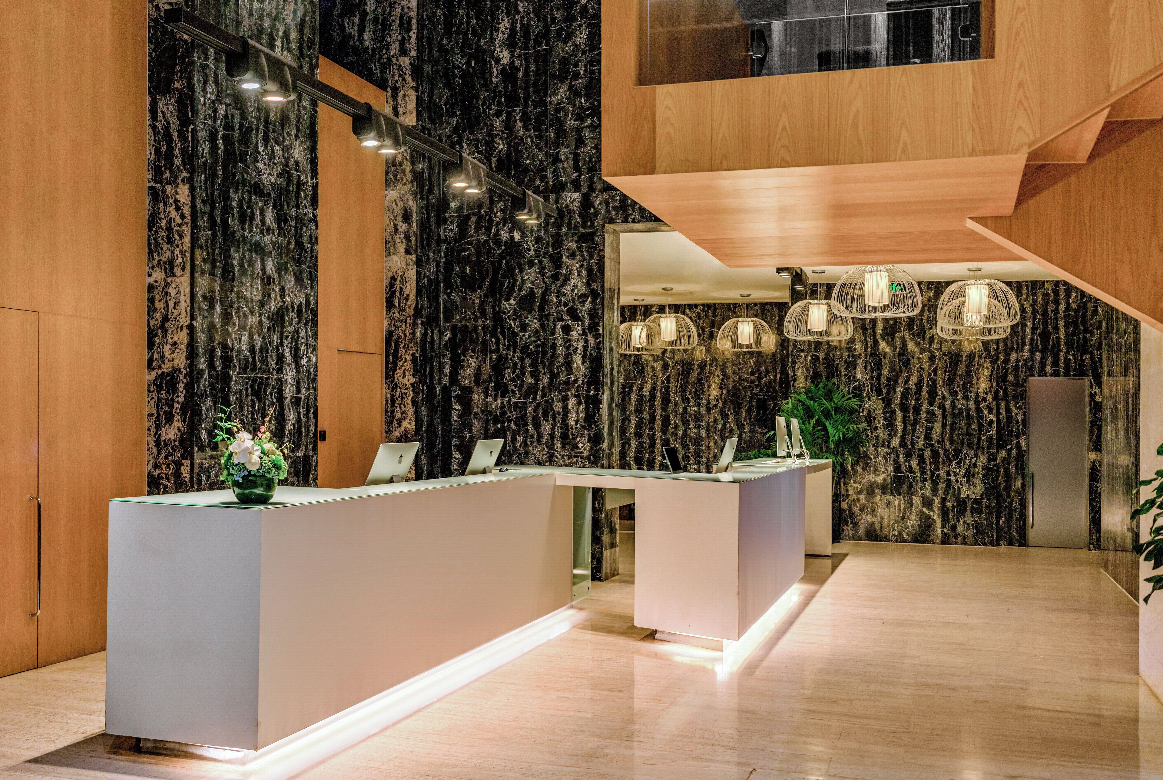 A modern reception area with a marble wall, a wooden reception desk, and pendant lighting.