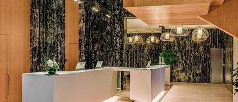 A modern reception area with a marble wall, a wooden reception desk, and pendant lighting.