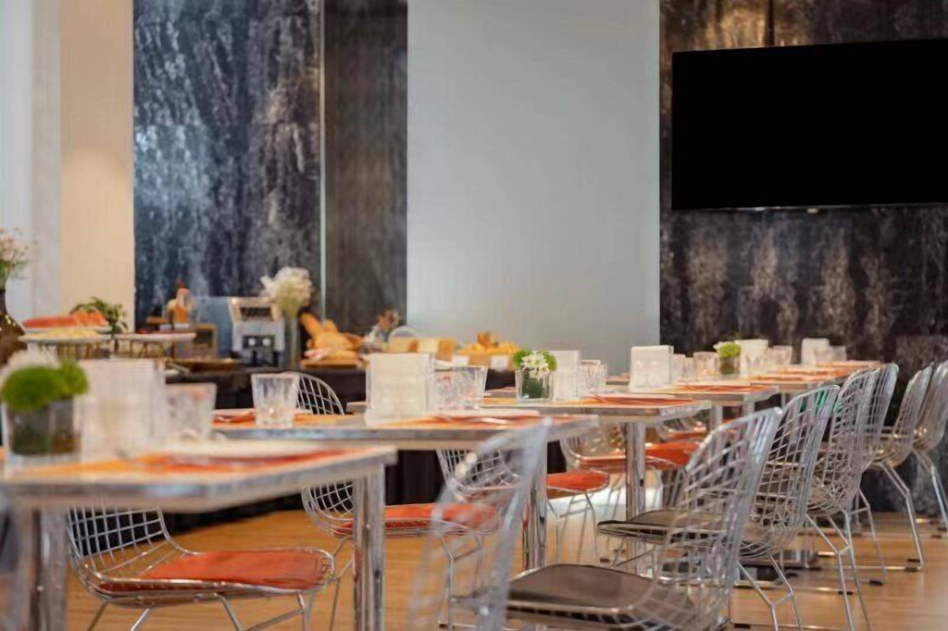 A dining area with tables set for service, clear chairs, and a large flat-screen TV mounted on the wall.