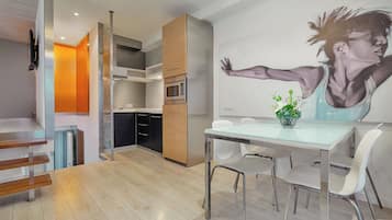 Une cuisine moderne équipée d’un four à micro-ondes, d’un four et de meubles en bois. On y trouve également un coin repas avec une table en verre et des chaises blanches.