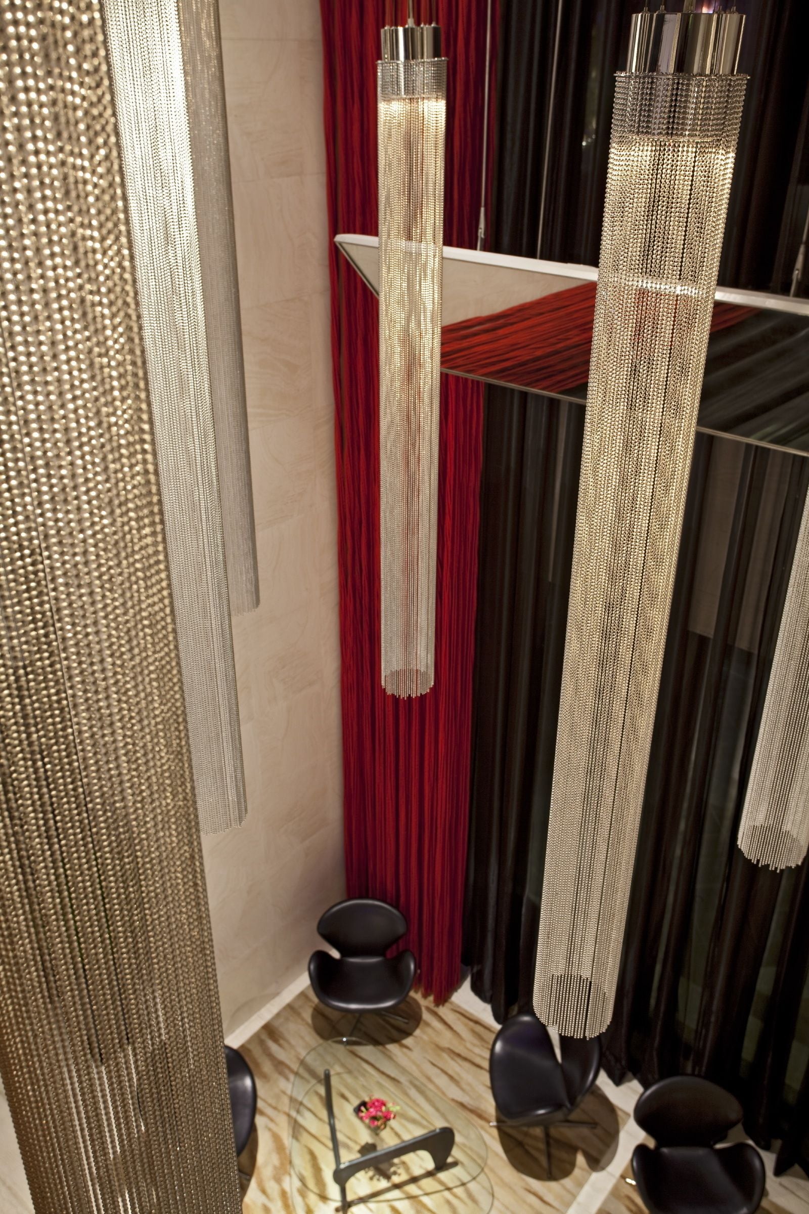 Ein modernes Interieur mit hohen, strukturierten Säulen, einem roten Vorhang und einem Glastisch mit Stühlen.