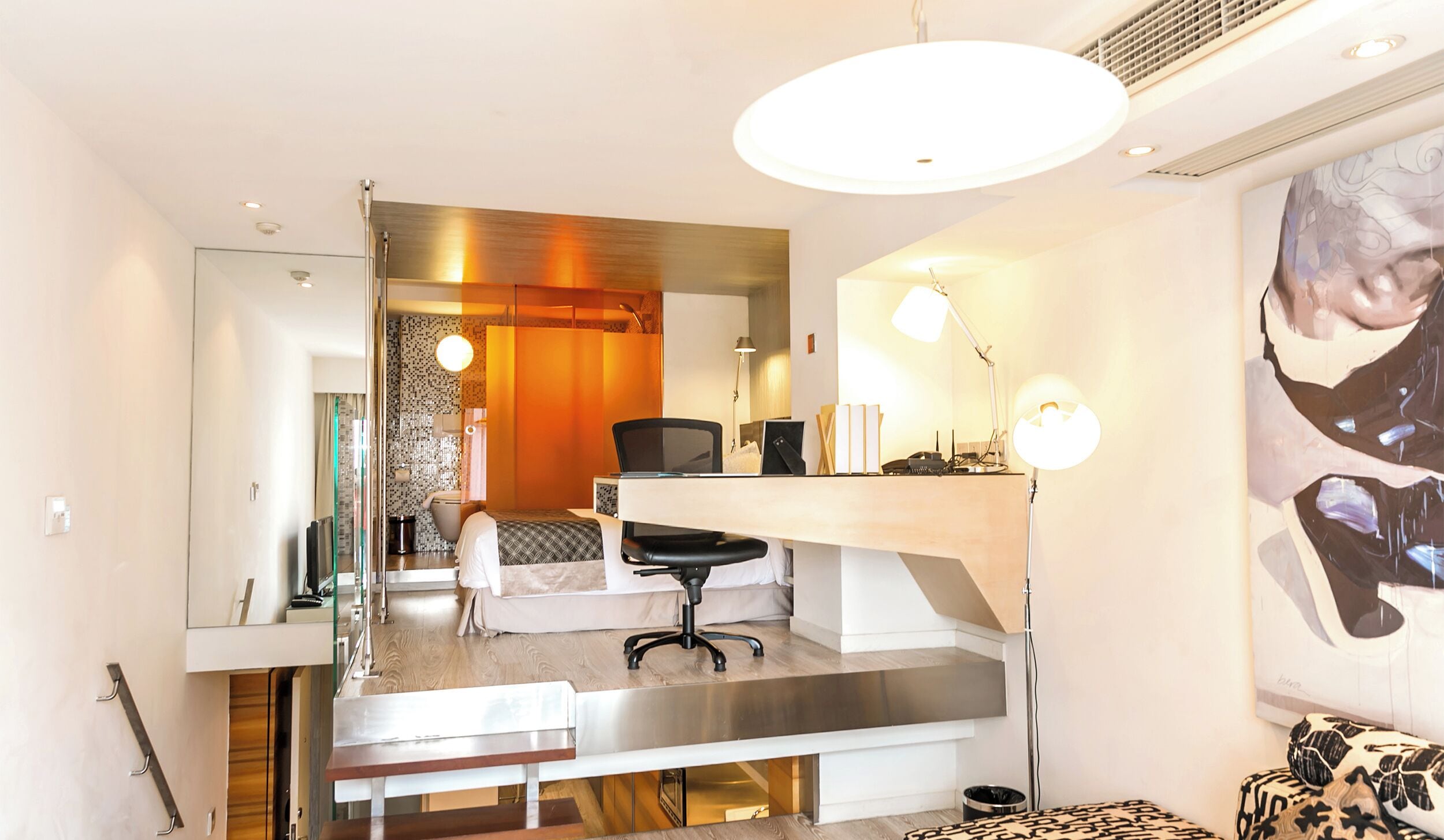 Een moderne hotelkamer met een bed, bureau, stoel en een grote spiegel.