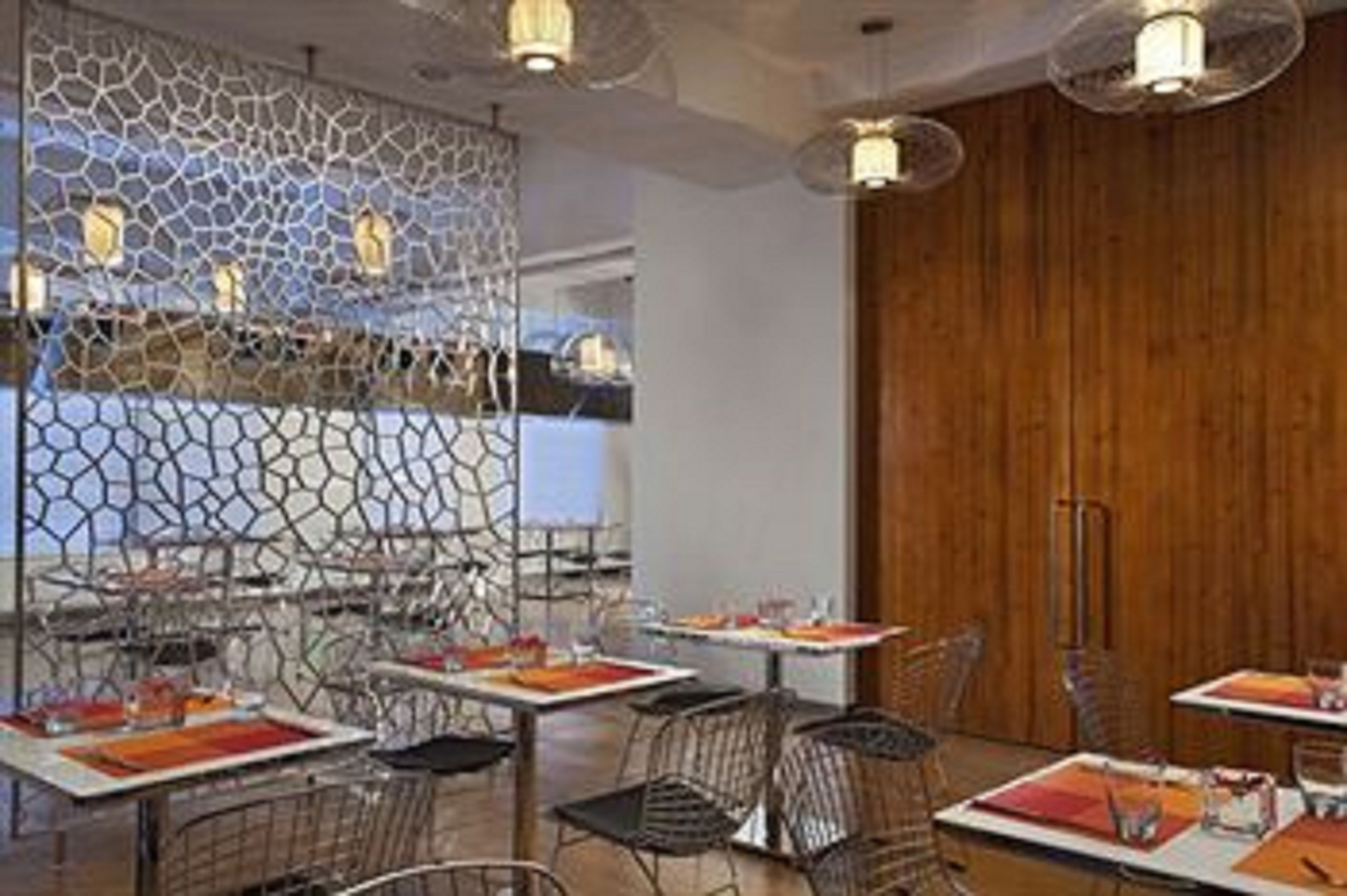 A restaurant with tables set for dining, a wooden wall, and hanging lights.