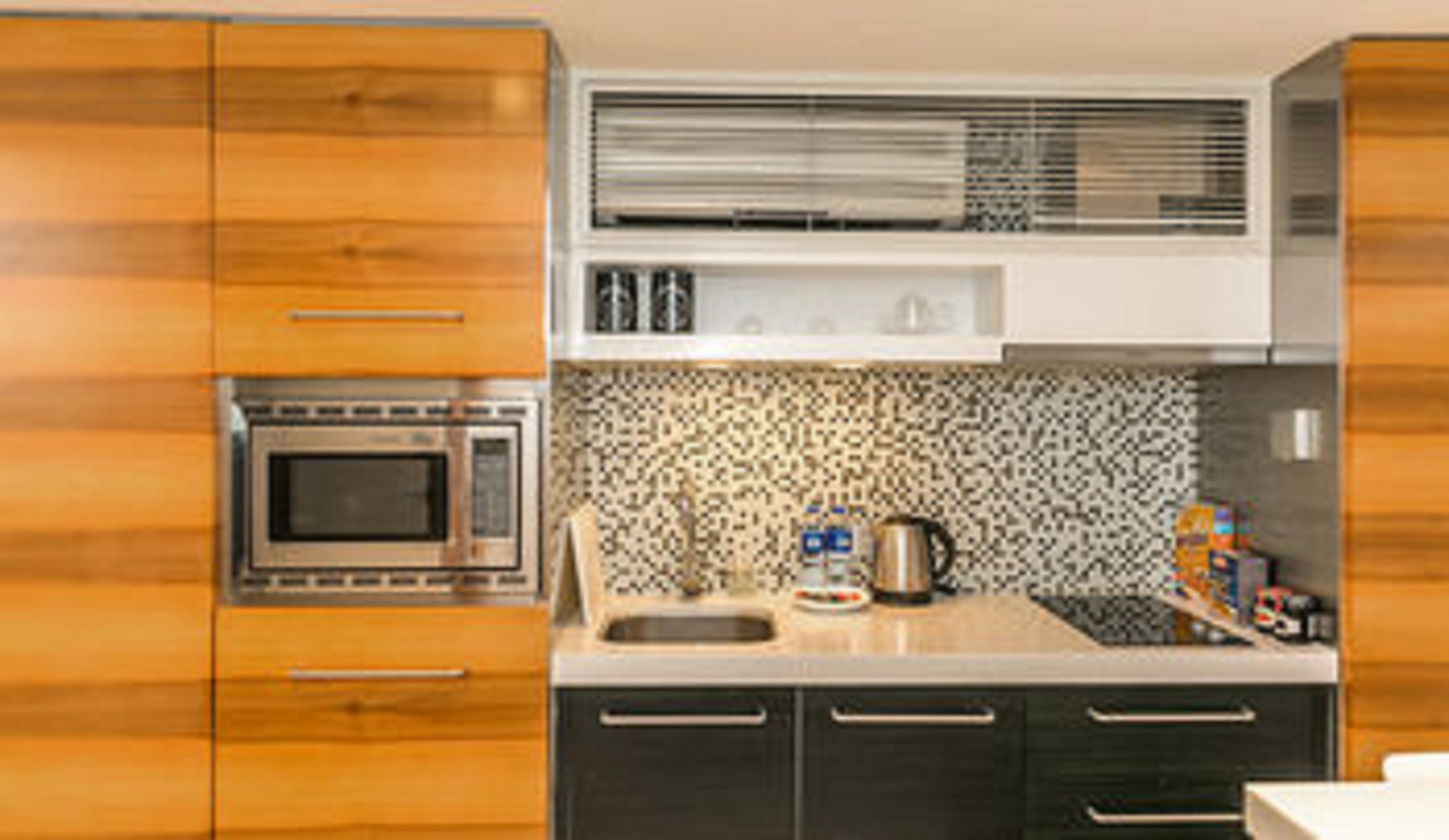A modern kitchen with wooden cabinets, a microwave, a sink, and a patterned backsplash.