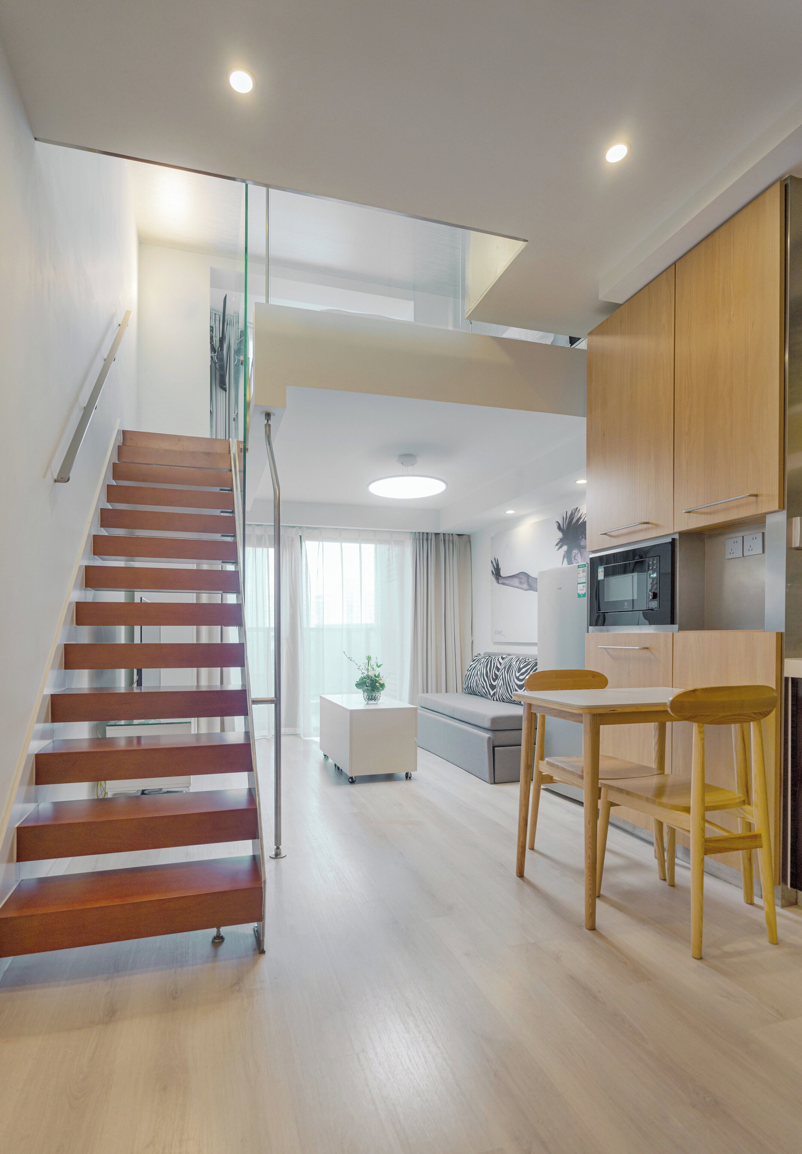 A modern apartment with a wooden staircase, a kitchen with wooden cabinets, a dining area with a table and chairs, and a living room with a sofa and a plant.