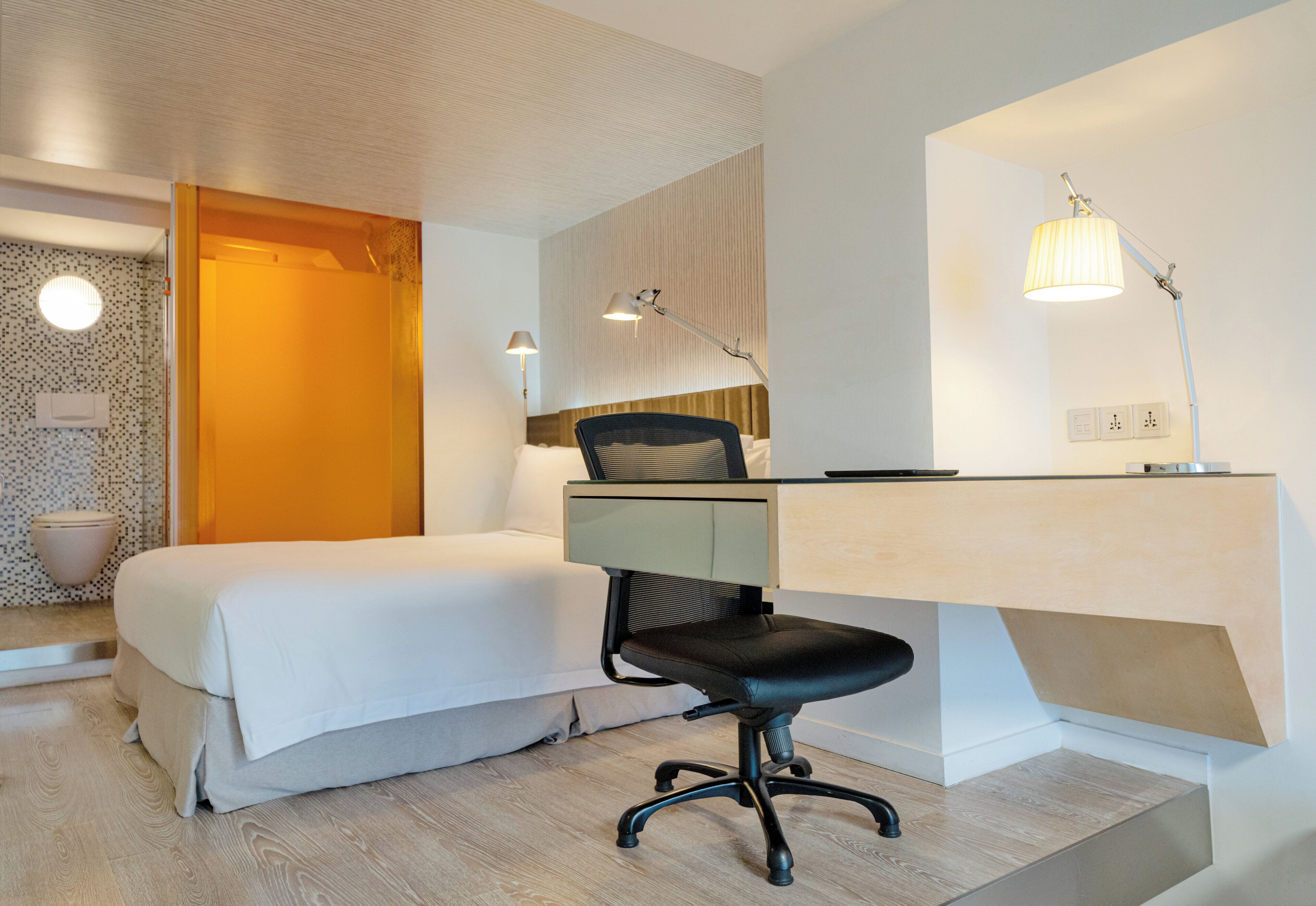 Una habitación de hotel moderna con una cama, escritorio, silla y dos lámparas.