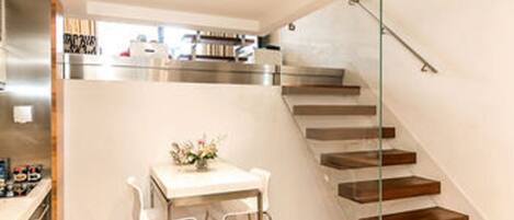 A modern kitchen with stainless steel appliances, a dining area with a table and chairs, and a staircase with wooden steps.