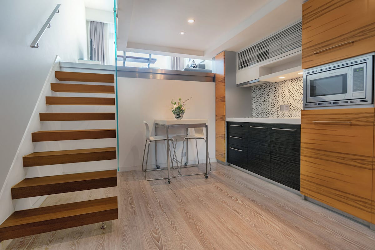 Une cuisine moderne avec un escalier en bois, un coin repas avec une petite table et des chaises, et un four à micro-ondes.
