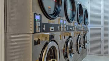 A row of four front-loading washers with control panels, located in a well-lit room with a tiled floor.
