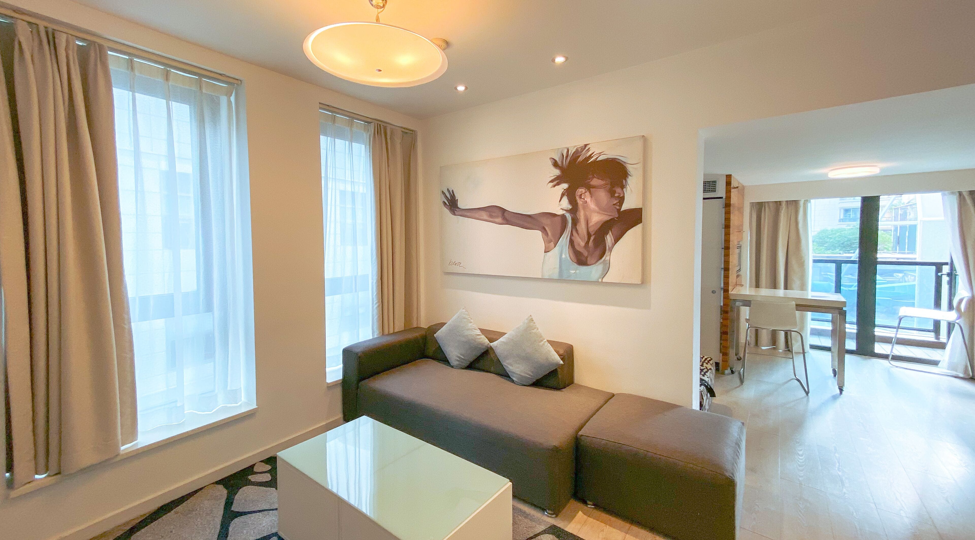 A modern living room with a sofa, a painting, and a dining area.