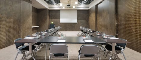Une salle de conférence avec une longue table, de nombreuses chaises, un écran de projection et un sol recouvert de moquette.