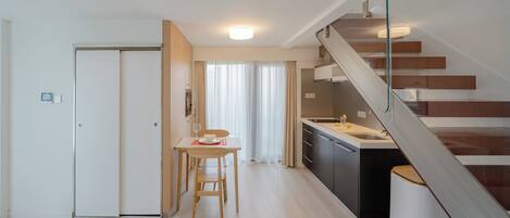 A modern kitchen with a dining area, a staircase, and a white door.