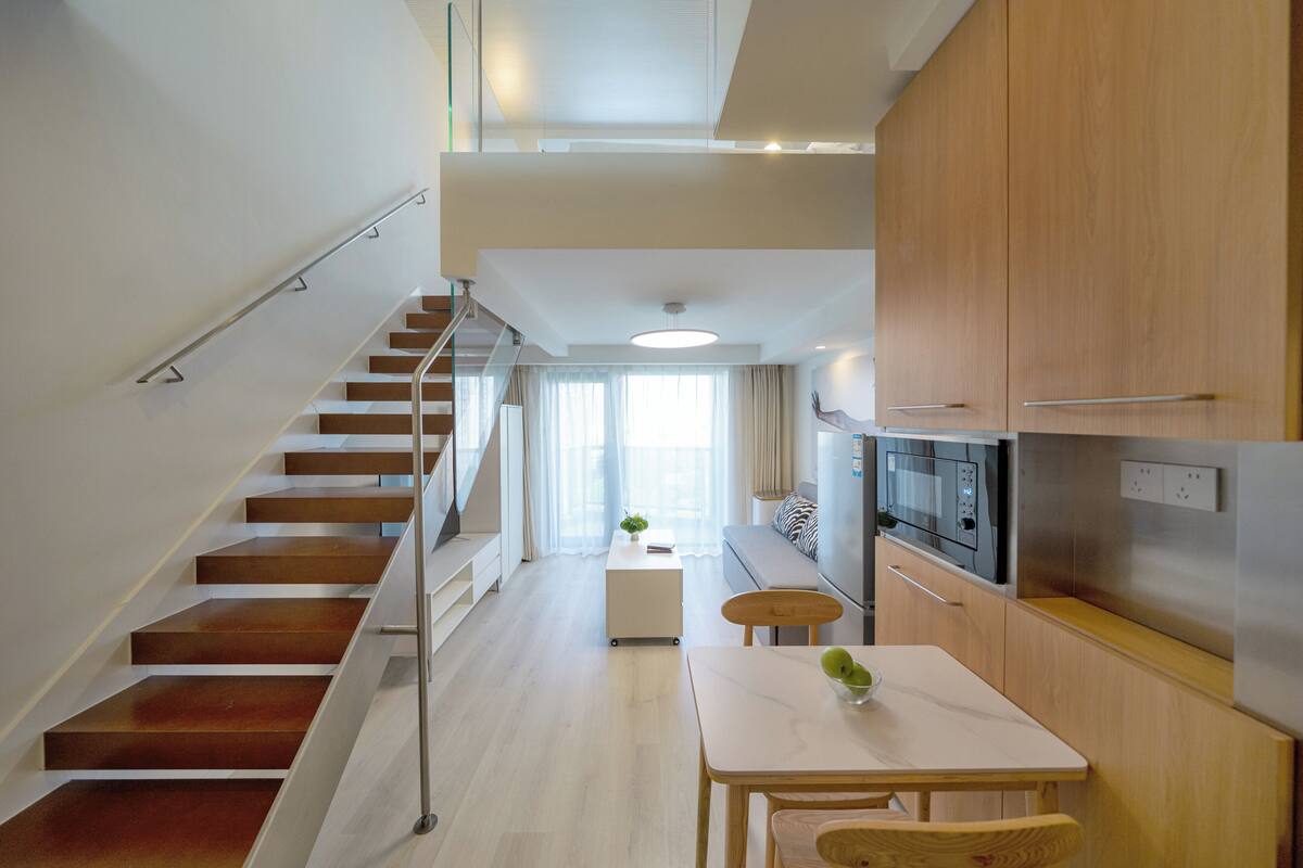 Une cuisine moderne avec des meubles en bois, une table à manger et un escalier menant à une mezzanine.