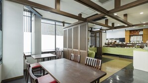Restaurante com vigas de madeira, balcão com toalha de mesa verde e área de cozinha ao fundo.