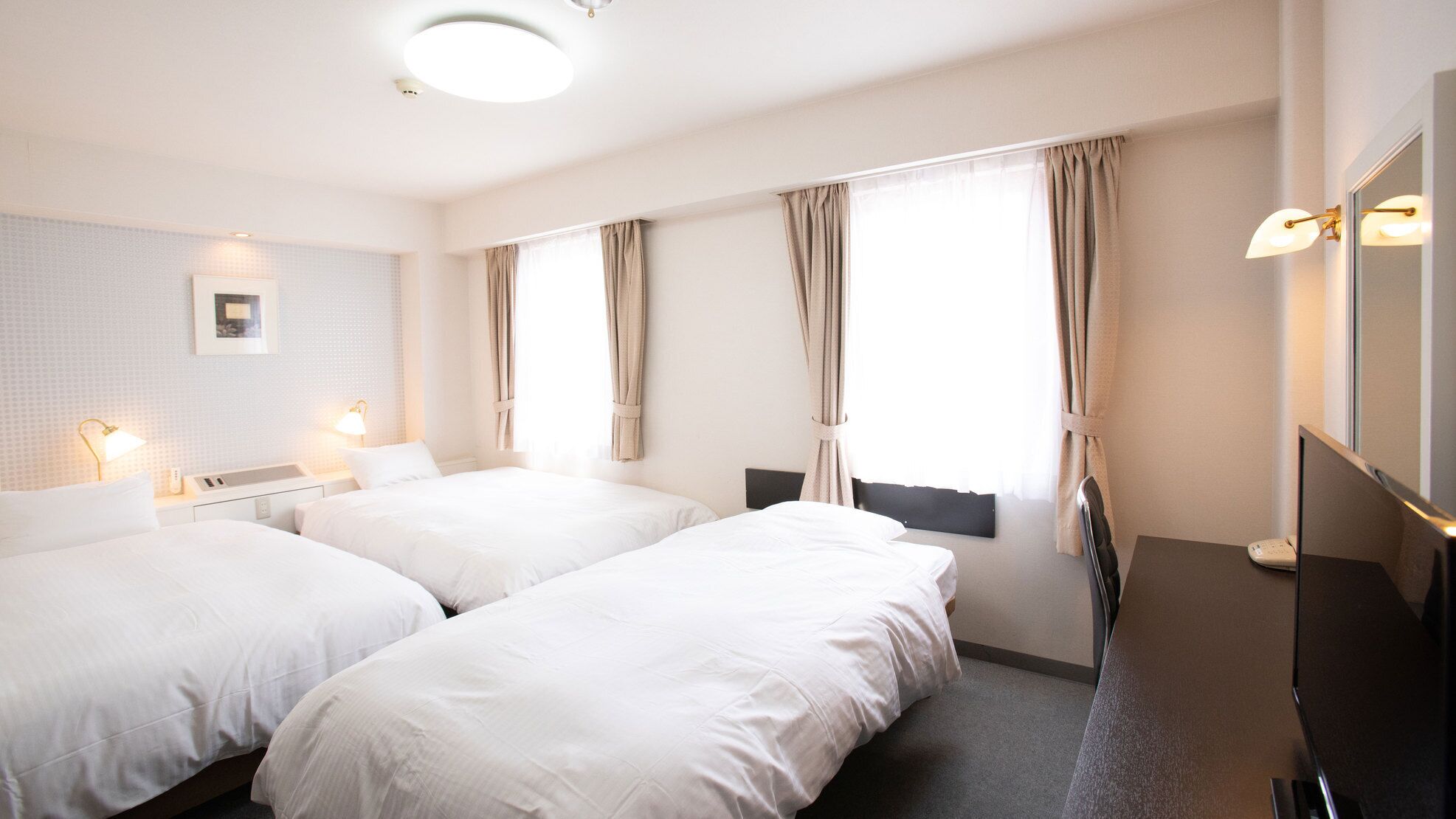 Une chambre d’hôtel avec deux lits, une table de chevet avec une lampe, un miroir et une fenêtre avec des rideaux.